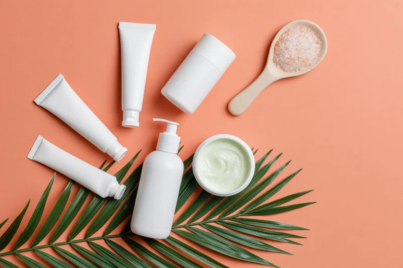 White unlabeled skincare products arranged with a palm leaf on an orange background