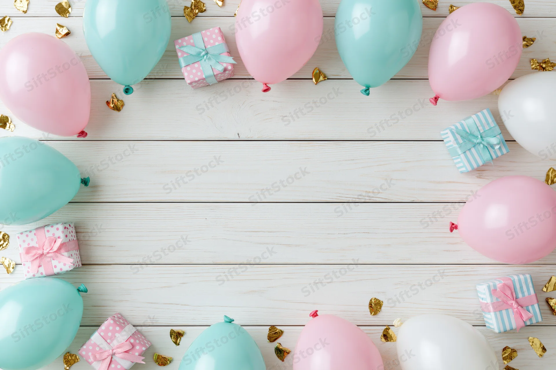 Pastel balloons and wrapped gifts arranged around a white wooden surface with gold confetti for a birthday party flat lay