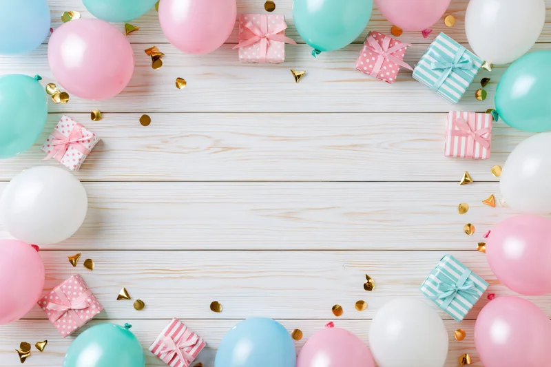 Pastel balloons and gift boxes arranged in a frame on a white wooden table with copyspace in the center
