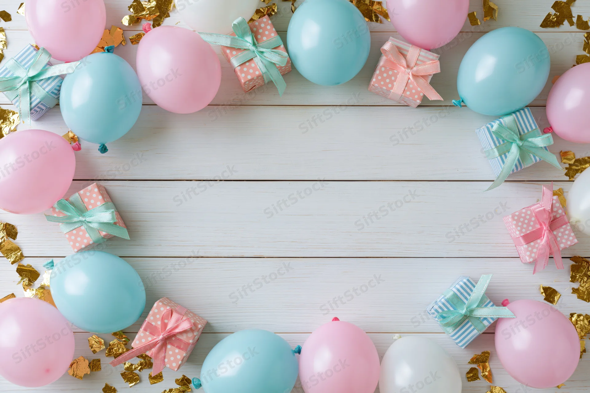 Pastel balloons and gift boxes arranged in a border around a white wooden surface with gold confetti and copyspace in the center