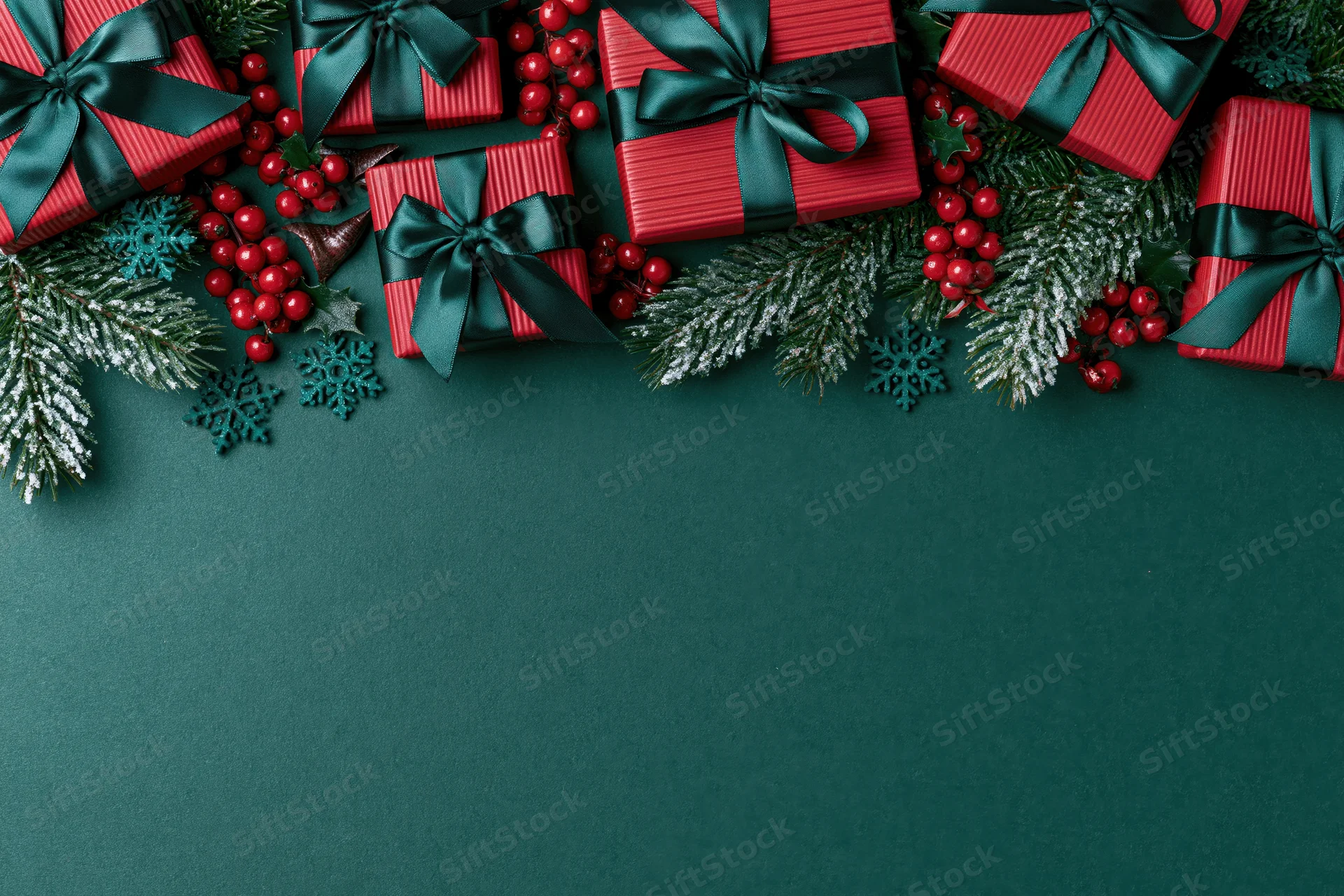 Red striped gift boxes with dark green ribbons and pine branches arranged along the top of a dark green surface, leaving copyspace below