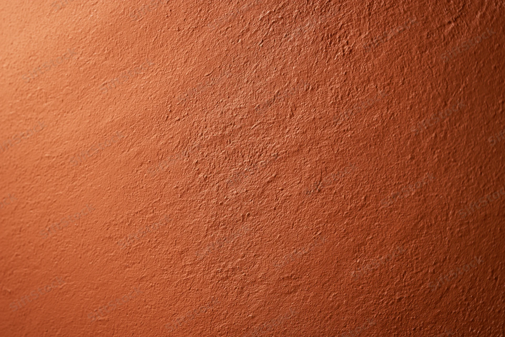 Textured stucco wall painted in deep burnt orange, filling the frame with warm earthy tone and subtle gradient lighting