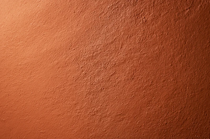 Textured stucco wall painted in deep burnt orange, filling the frame with warm earthy tone and subtle gradient lighting