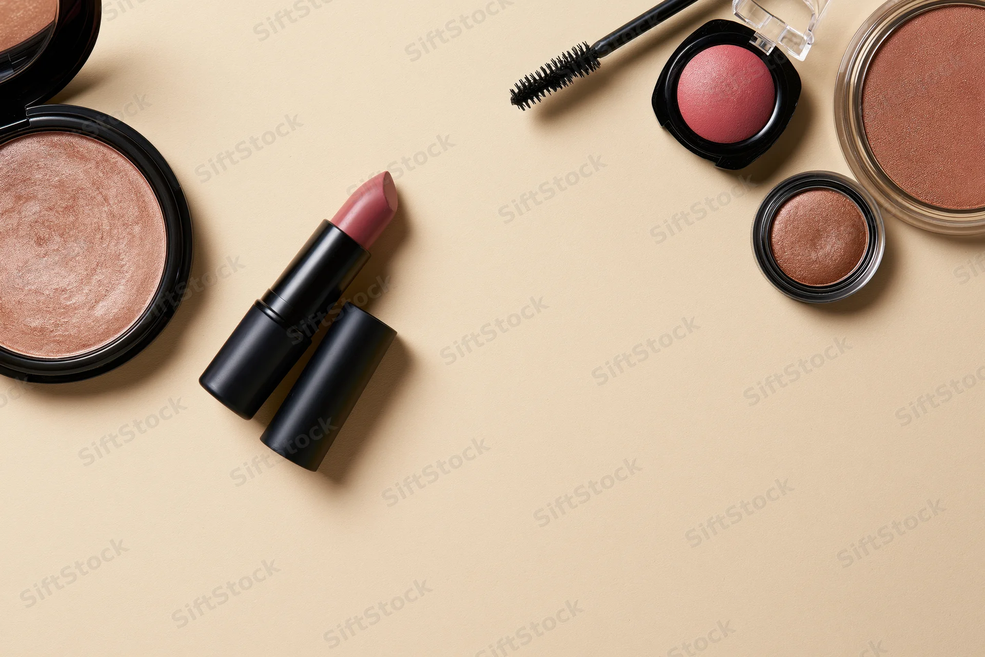 Makeup products arranged in flatlay on beige surface with copyspace