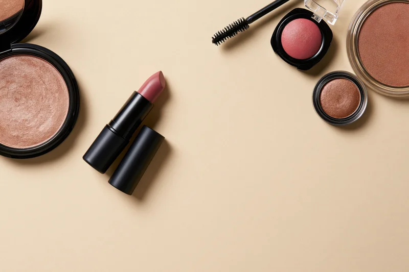 Makeup products arranged in flatlay on beige surface with copyspace