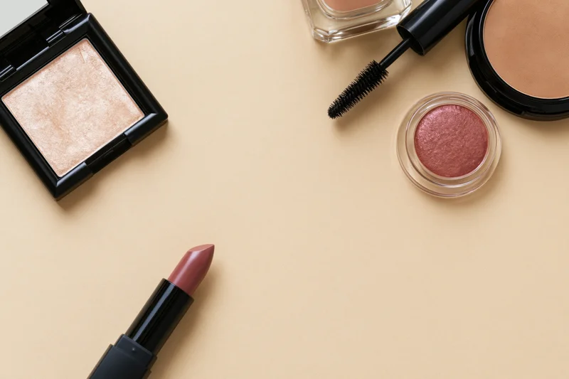 Makeup products arranged in flatlay on beige surface with copyspace