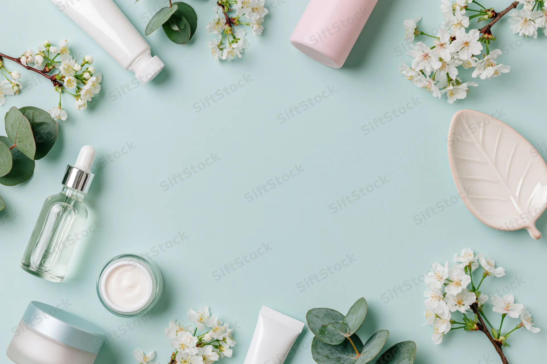 Skincare products and spring blossoms arranged in a border frame on a mint background