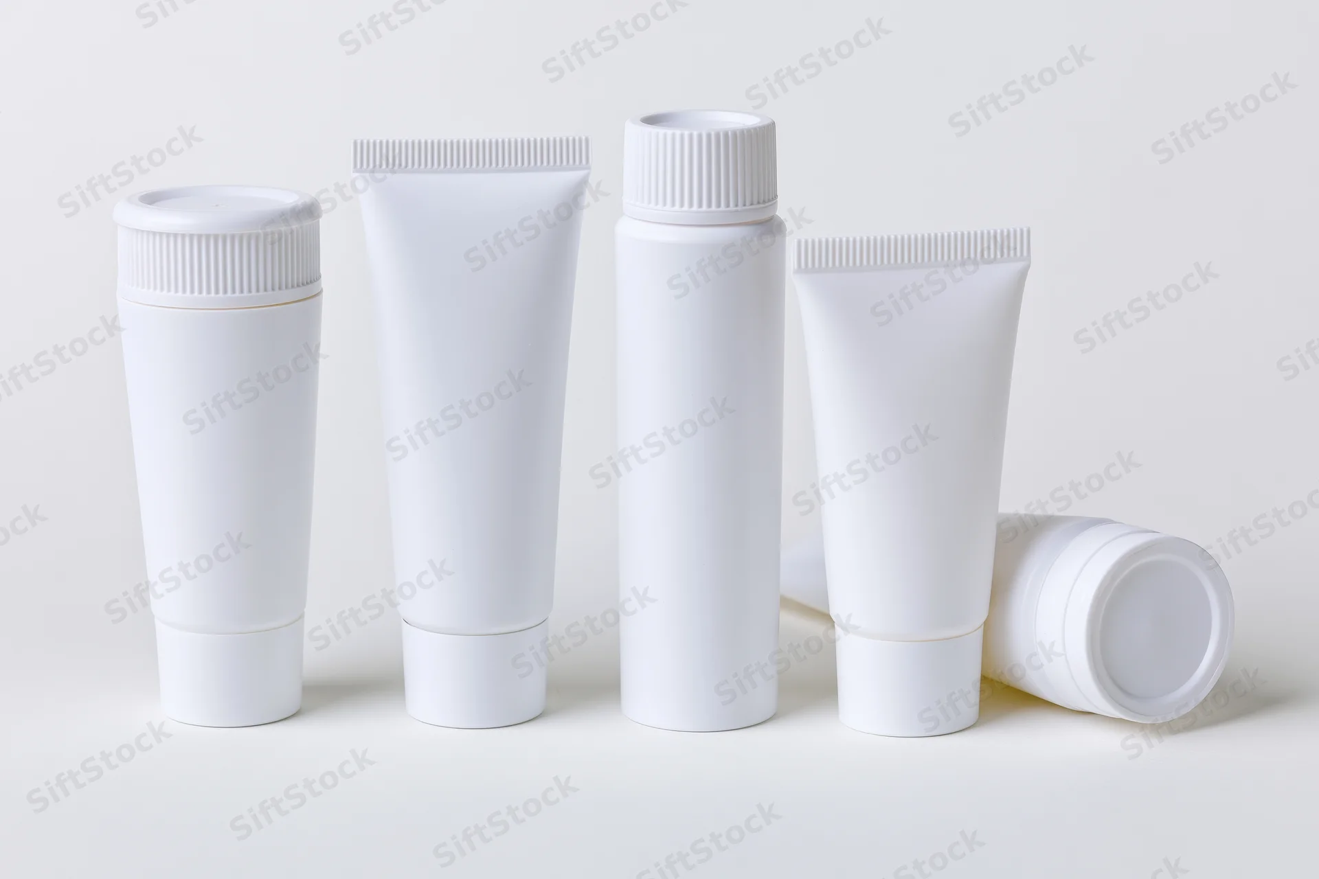 White plastic cosmetic squeeze tubes arranged in a row on a plain surface