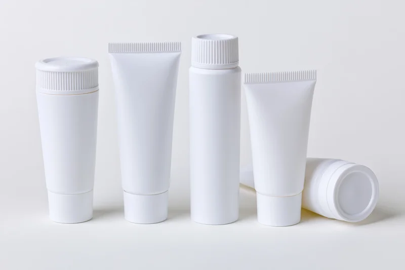 White plastic cosmetic squeeze tubes arranged in a row on a plain surface