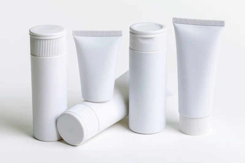 White plastic cosmetic squeeze tubes arranged in a row on a plain white surface