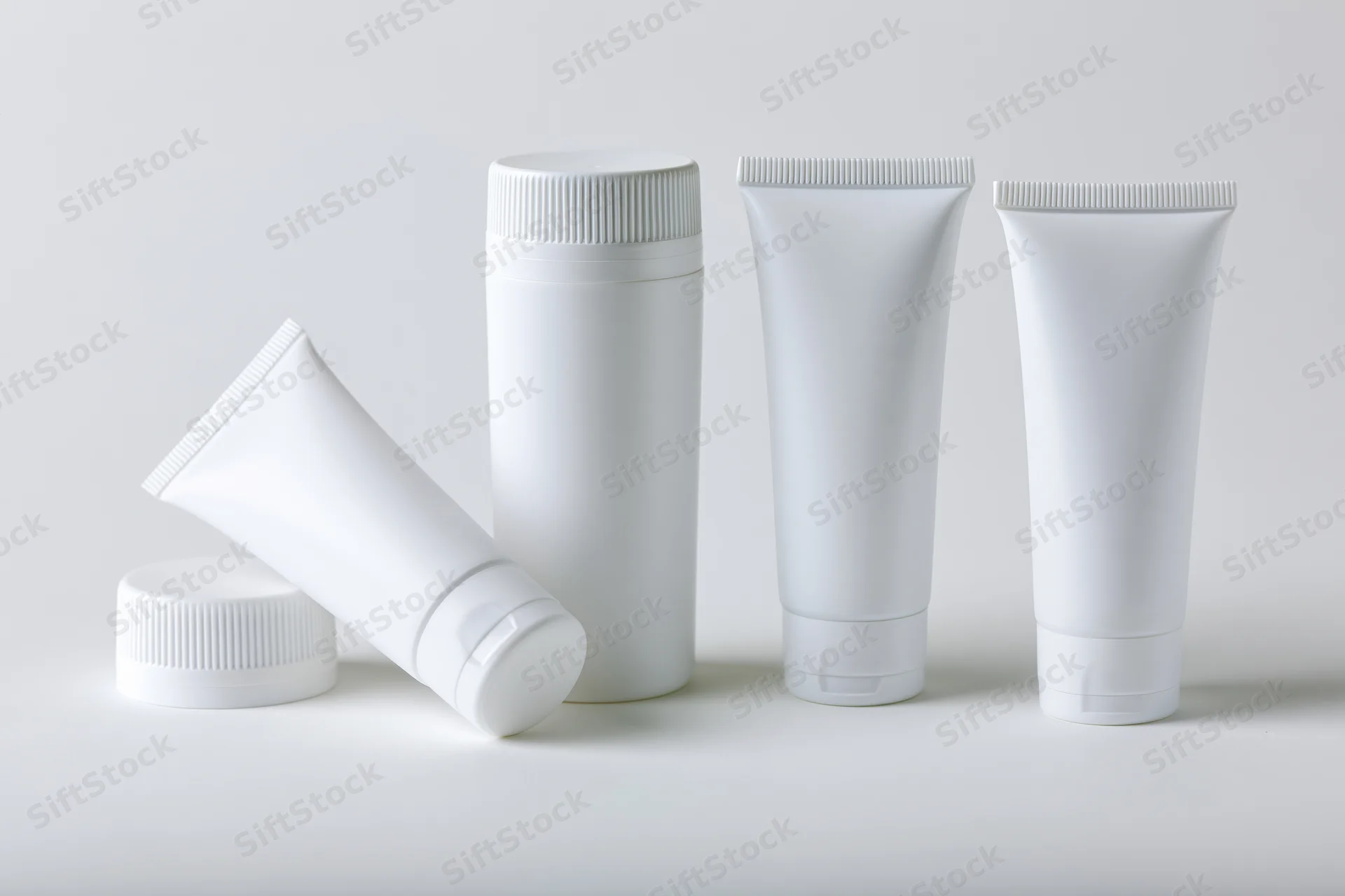 White plastic cosmetic squeeze tubes arranged in a row on a plain surface
