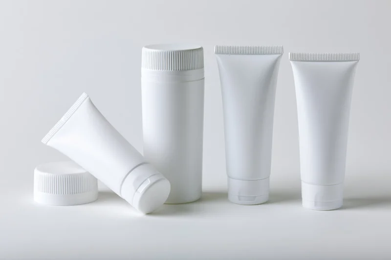 White plastic cosmetic squeeze tubes arranged in a row on a plain surface