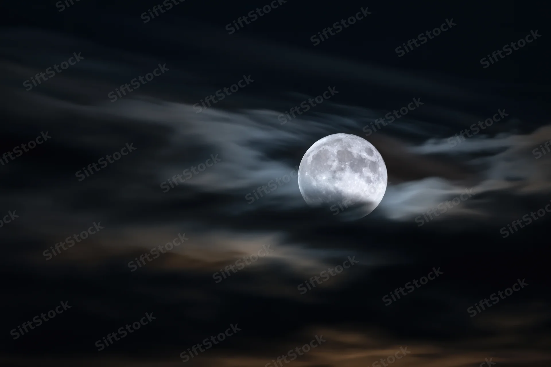 Full moon glowing through wispy clouds in dark night sky