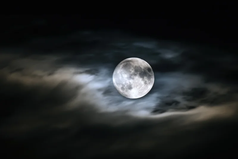 Full moon glowing through wispy clouds in dark night sky
