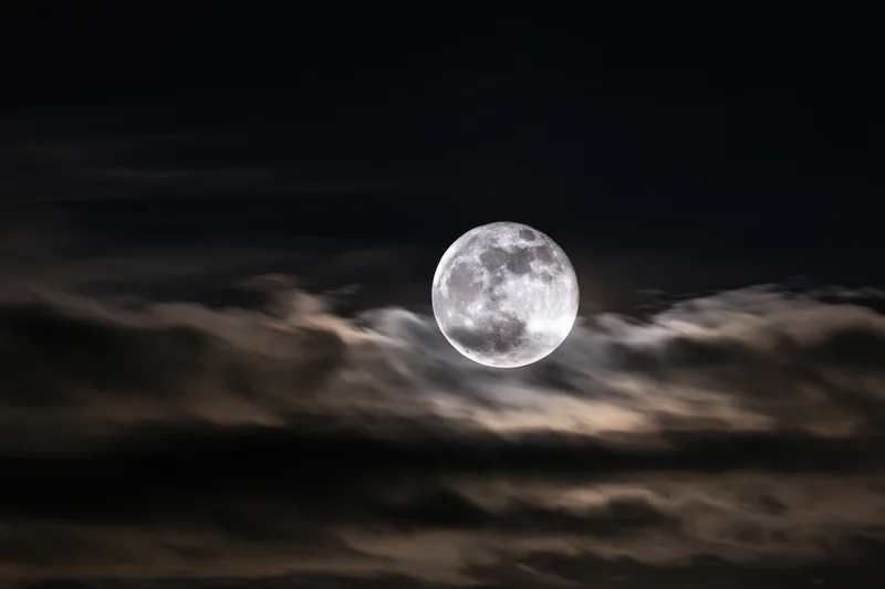 Full moon glowing above layered clouds in dark night sky