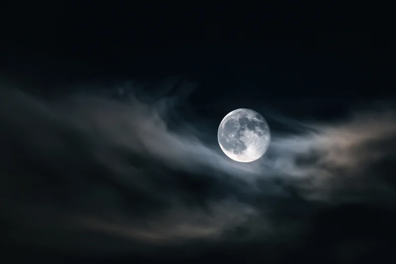 Full moon glowing through wispy clouds in dark night sky