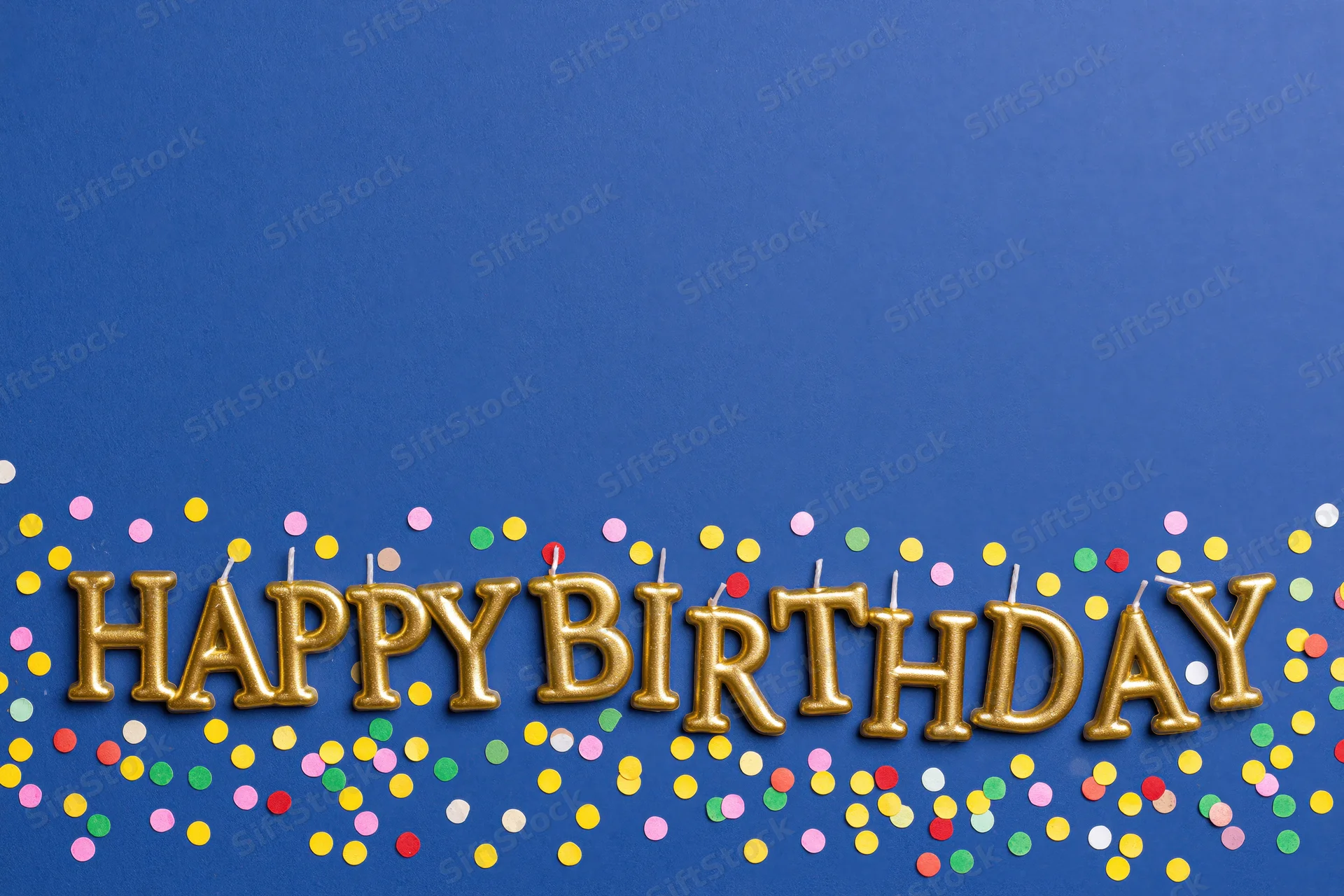Gold letter-shaped birthday candles spelling happy birthday on blue surface with colorful confetti