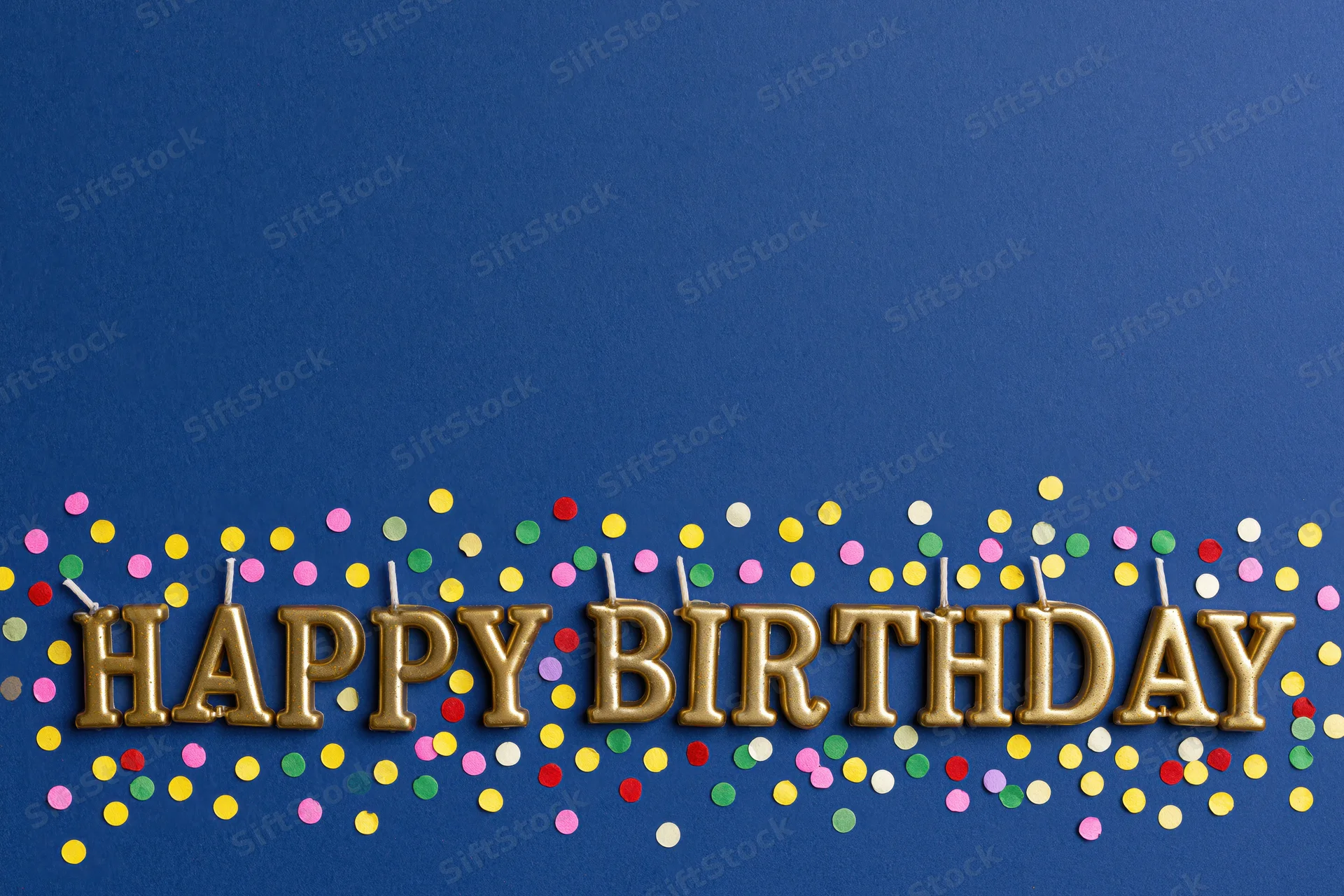Gold letter-shaped birthday candles spelling happy birthday on blue background with colorful confetti