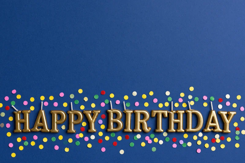 Gold letter-shaped birthday candles spelling happy birthday on blue background with colorful confetti
