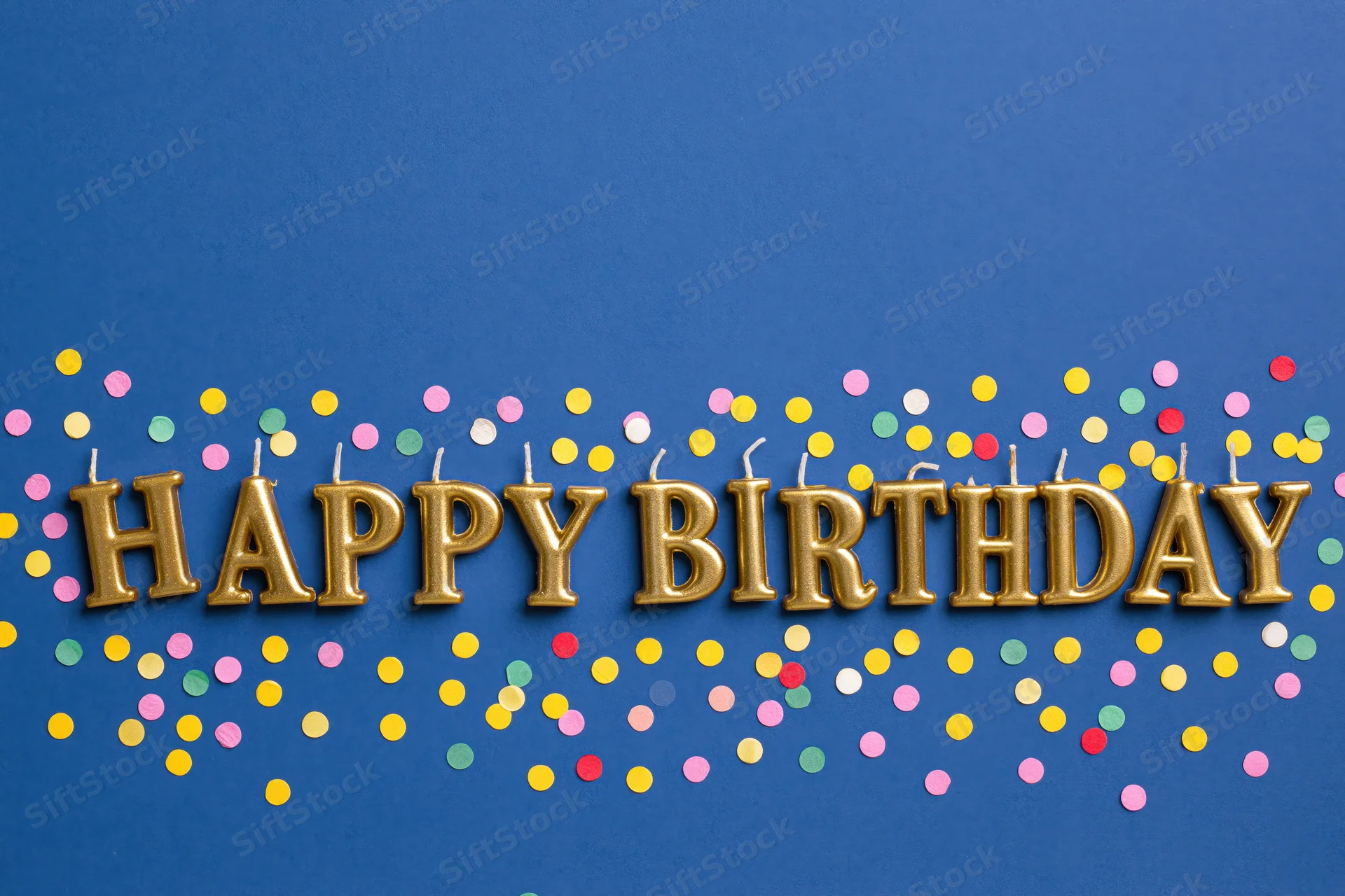 Gold letter-shaped birthday candles spelling happy birthday on blue background with colorful confetti