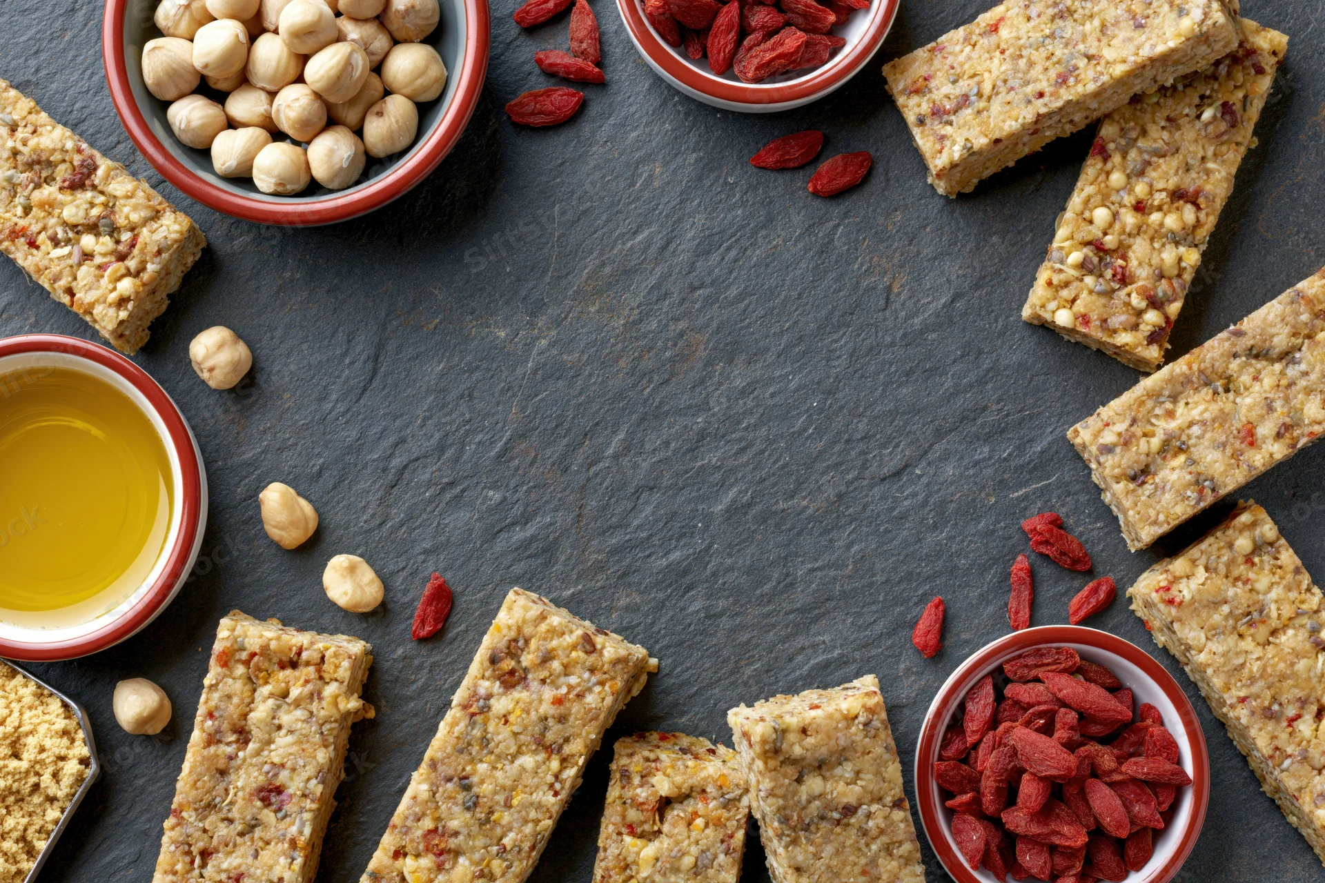 Granola bars and ingredients arranged in a loose frame on dark slate surface with copyspace in center