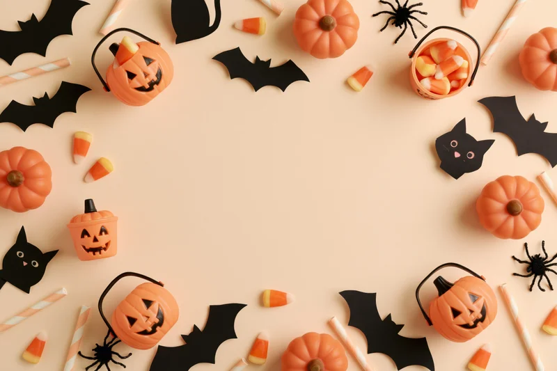 Halloween decorations arranged in a flat lay border around a central copyspace on a beige surface