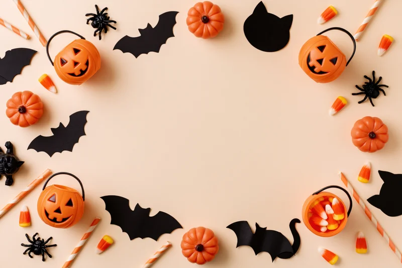 Halloween decorations arranged in a flat lay border around a central copyspace on a beige surface