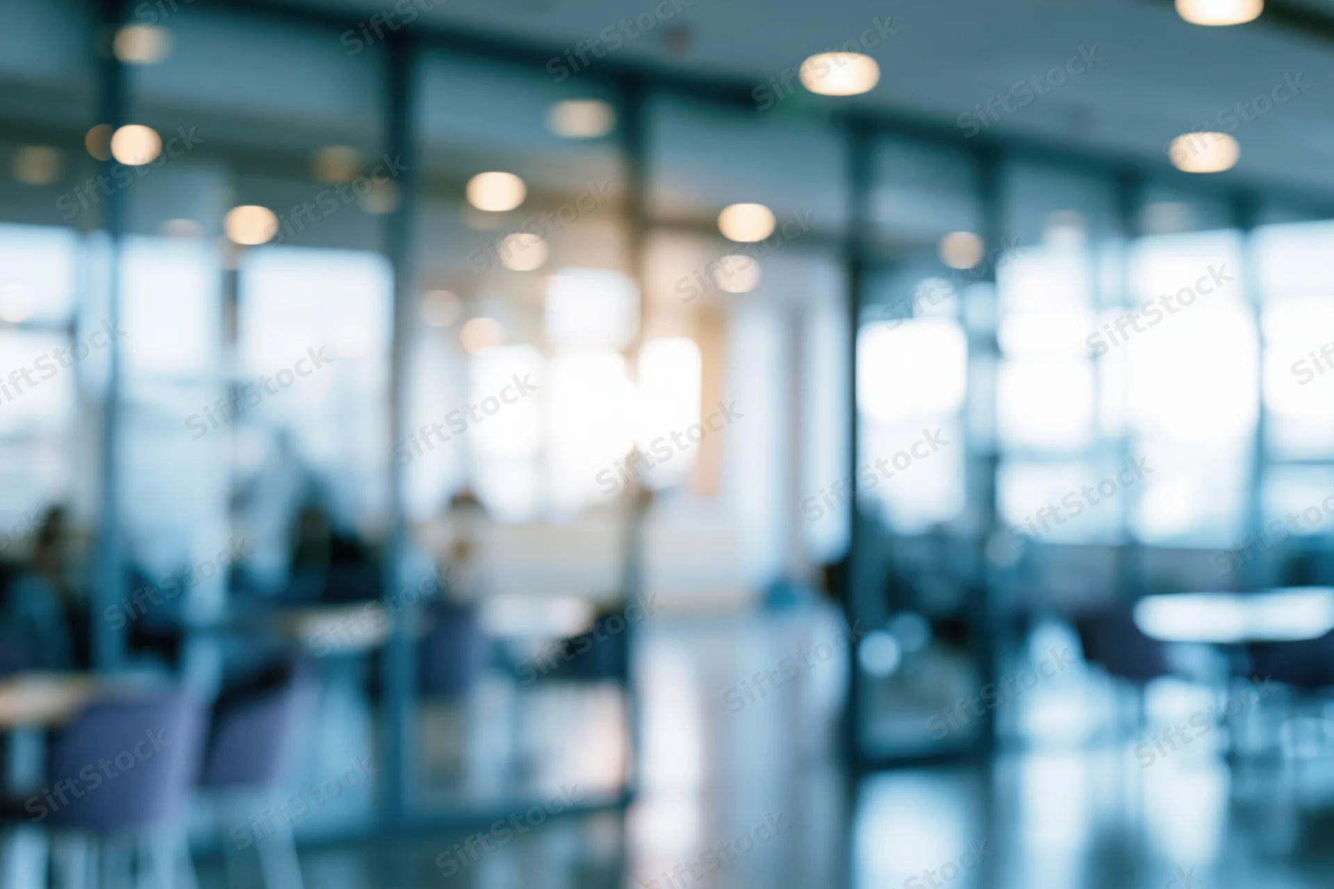 Blurred interior of a modern office lobby with glass partitions and ceiling lights