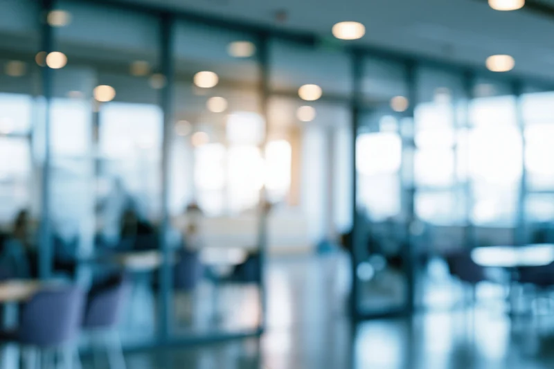 Blurred interior of a modern office lobby with glass partitions and ceiling lights