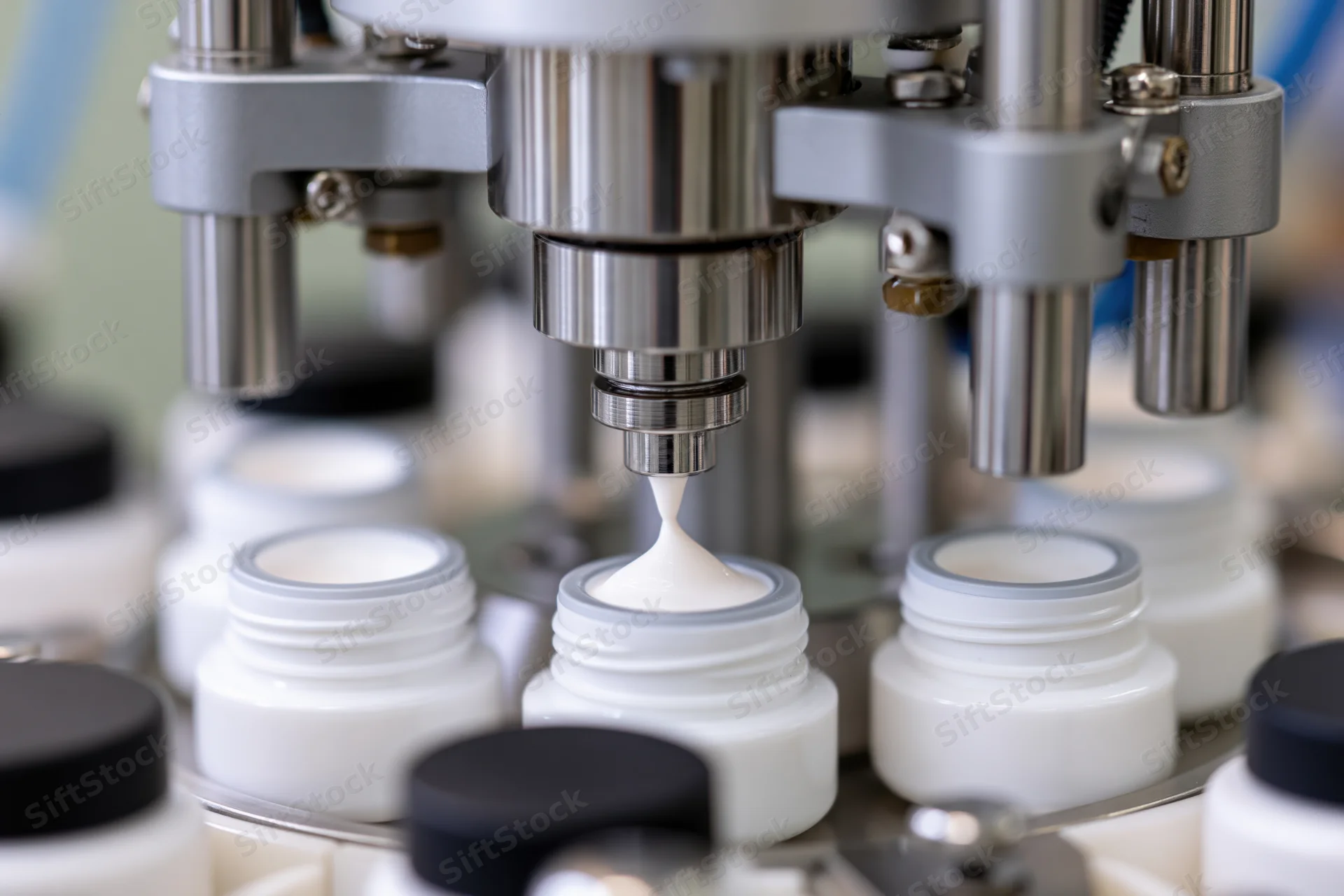 Industrial filling machine dispensing white cream into small bottles on a production line