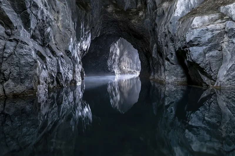 Flooded underground cave with still dark water reflecting rocky walls and entrance