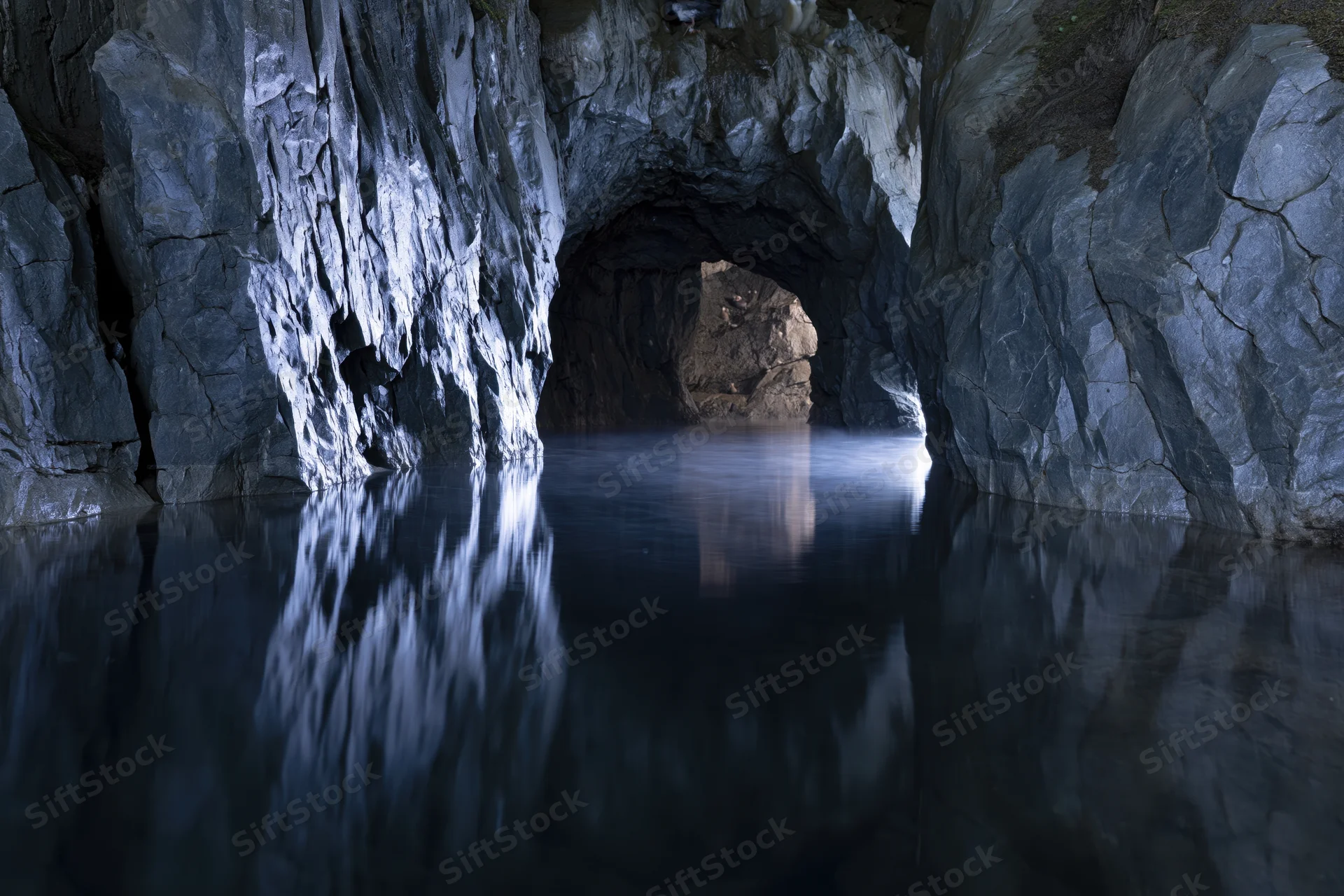 Flooded underground cave with still dark water reflecting rocky walls and tunnel entrance