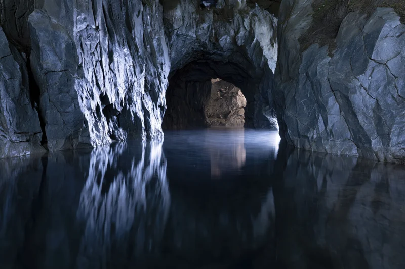 Flooded underground cave with still dark water reflecting rocky walls and tunnel entrance