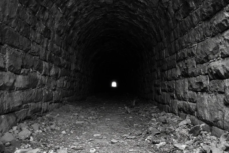 Stone railway tunnel interior with arched walls and light at far end