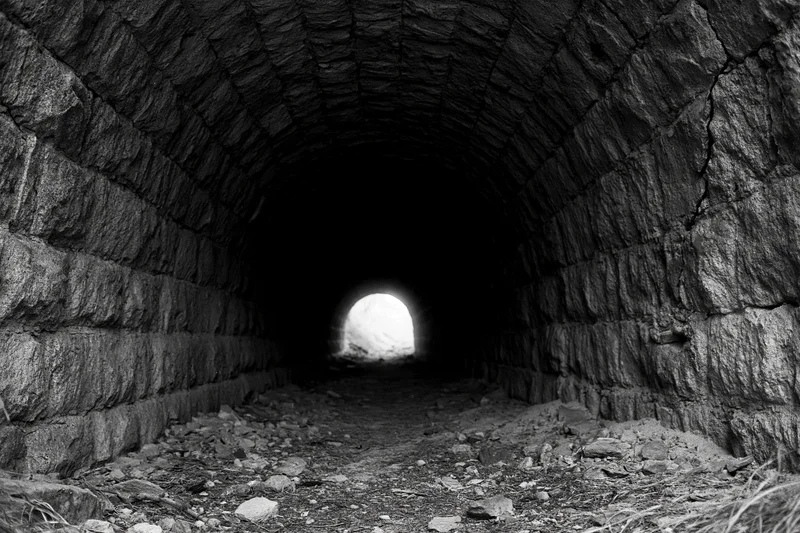 Stone railway tunnel interior with light at far end, abandoned and dark, rough masonry walls and rubble floor