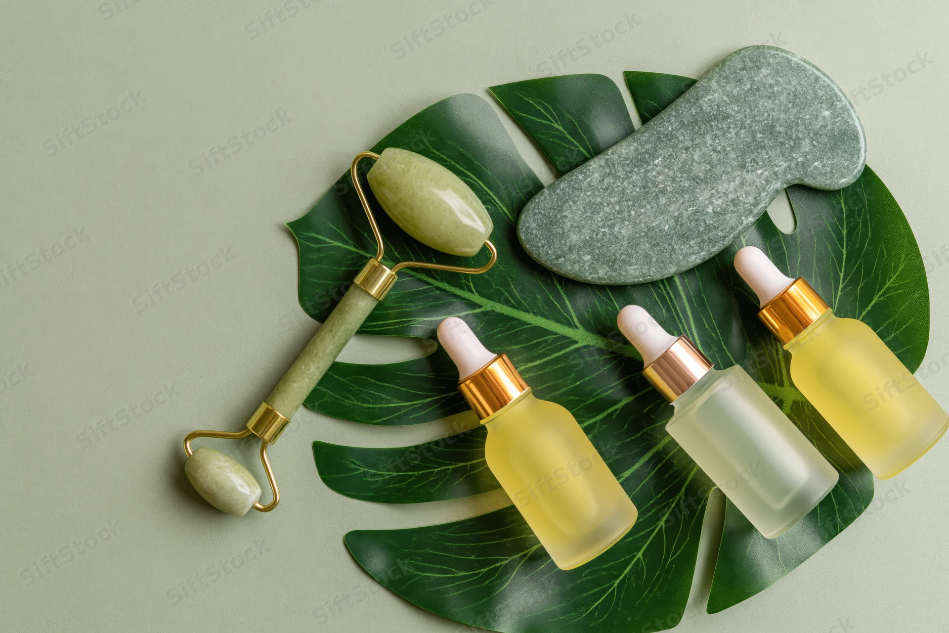 Jade facial roller and serum bottles arranged on a monstera leaf