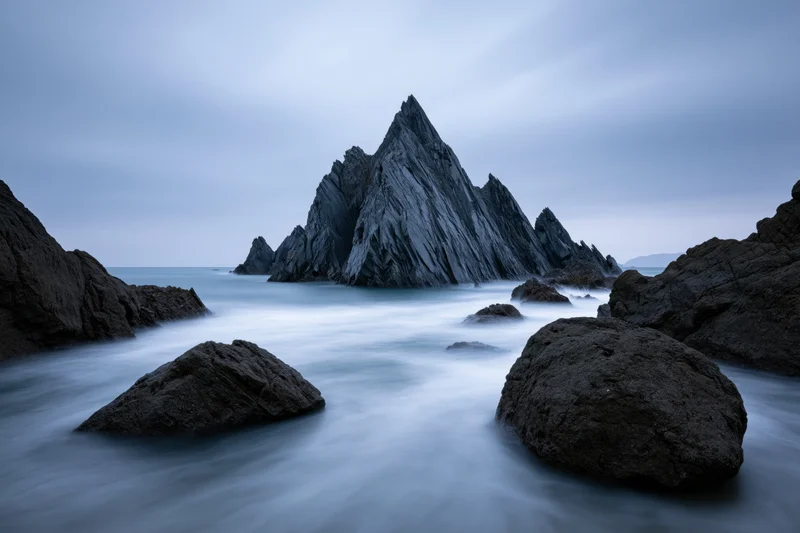 Jagged coastal rock formation rising from the sea under an overcast sky