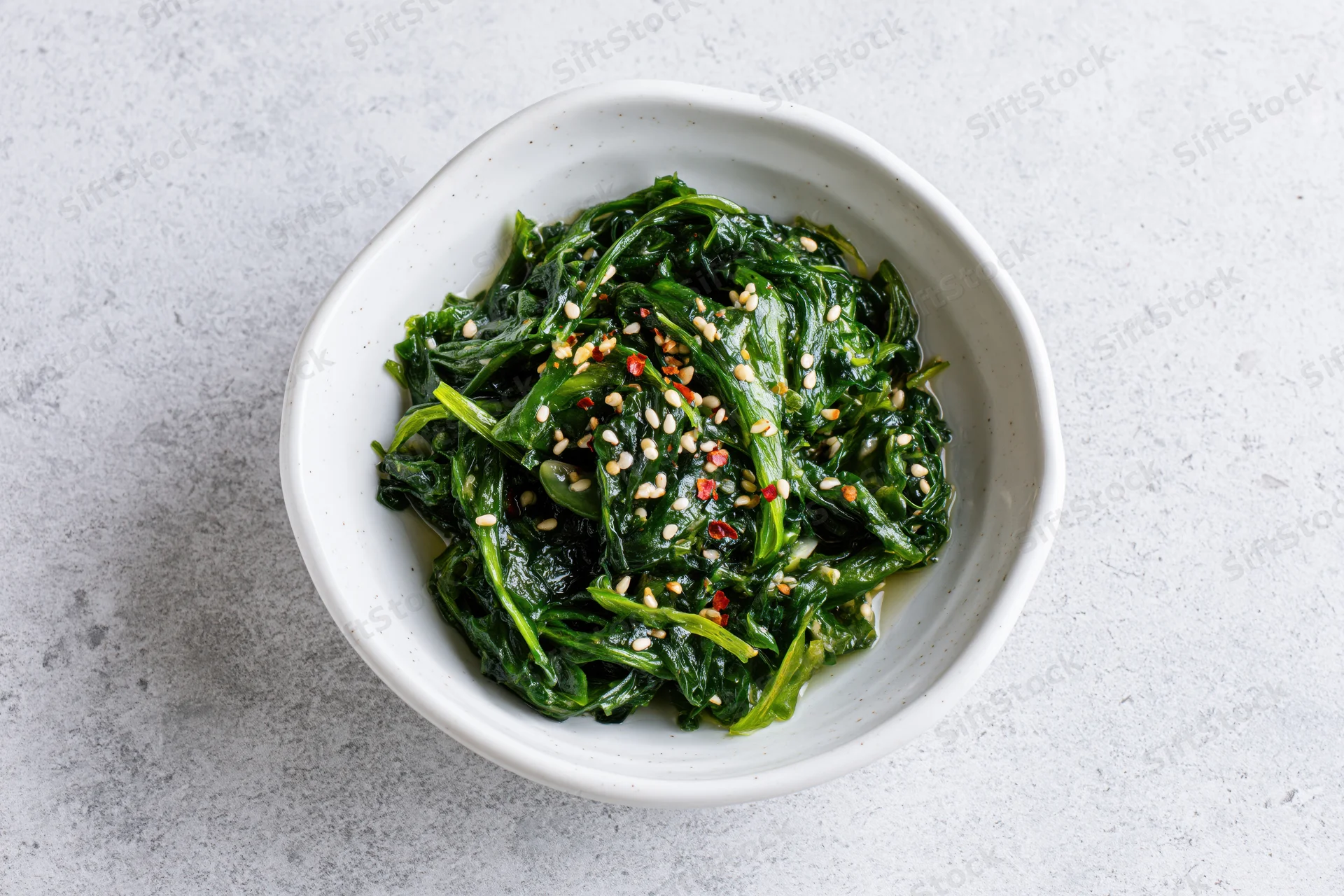 Wakame seaweed salad with sesame seeds and chili flakes in a white bowl on a light countertop