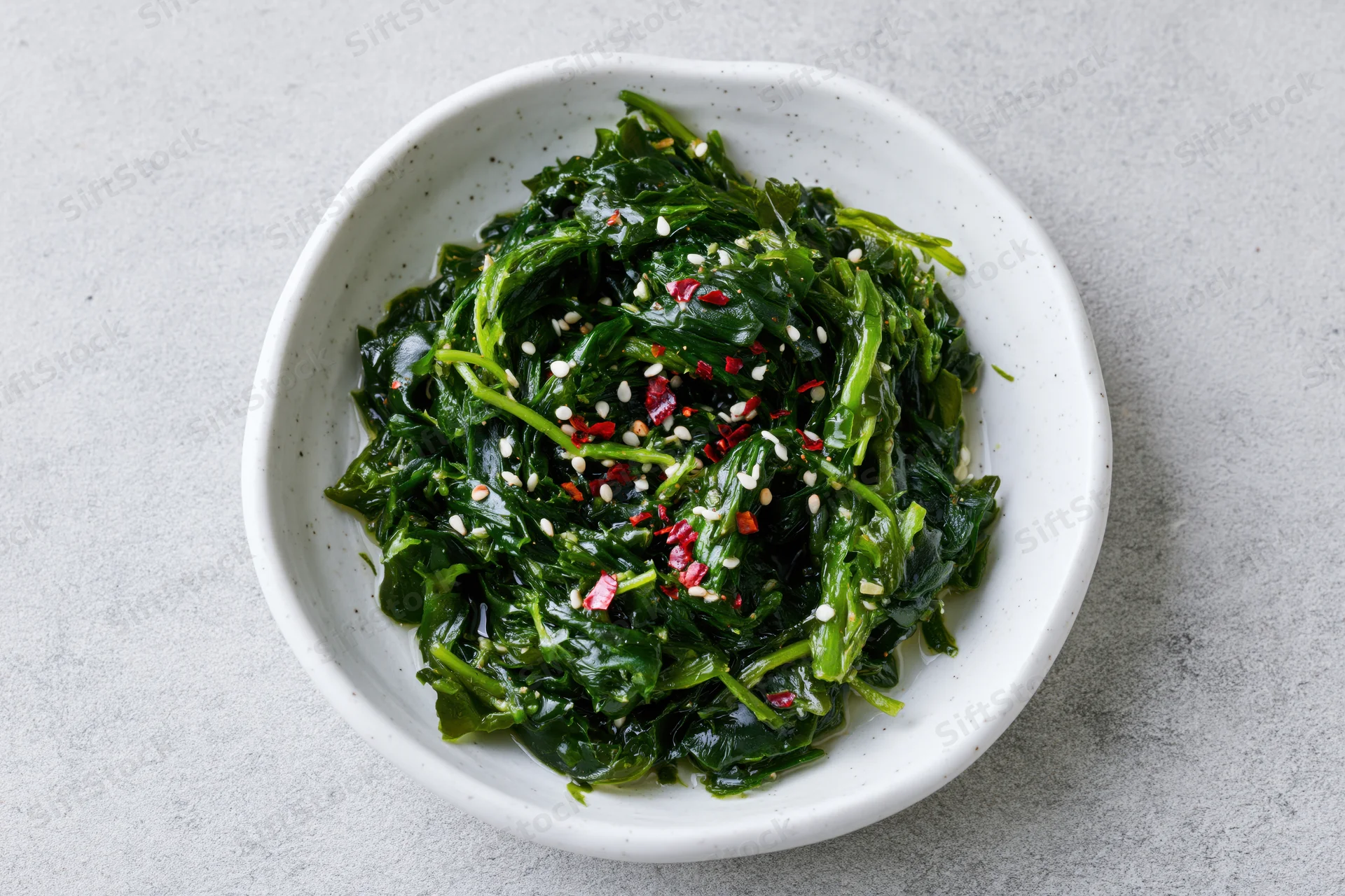 Wakame seaweed salad with sesame seeds and red chili in a white speckled bowl on a gray surface
