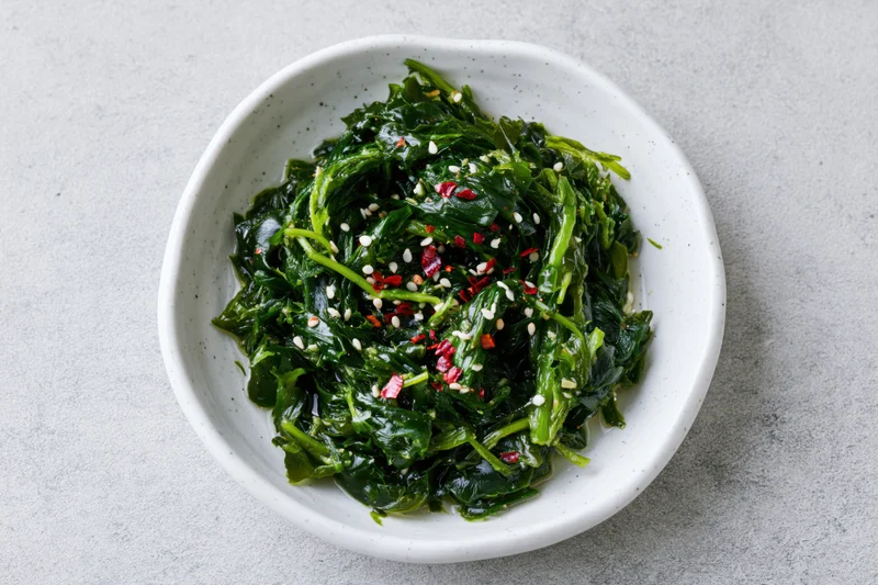 Wakame seaweed salad with sesame seeds and red chili in a white speckled bowl on a gray surface