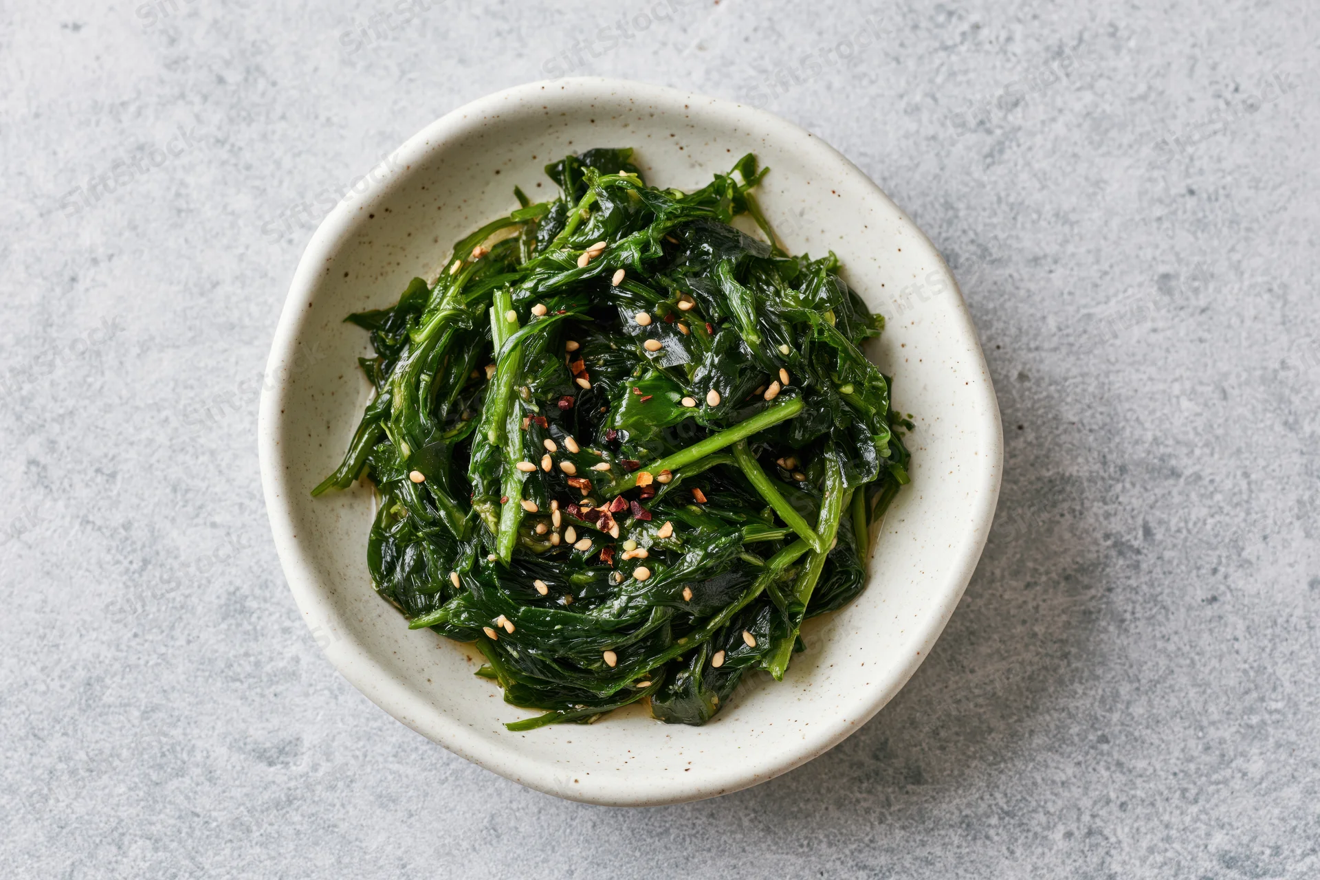 Wakame seaweed salad with sesame seeds and chili flakes in a white ceramic bowl on a gray surface