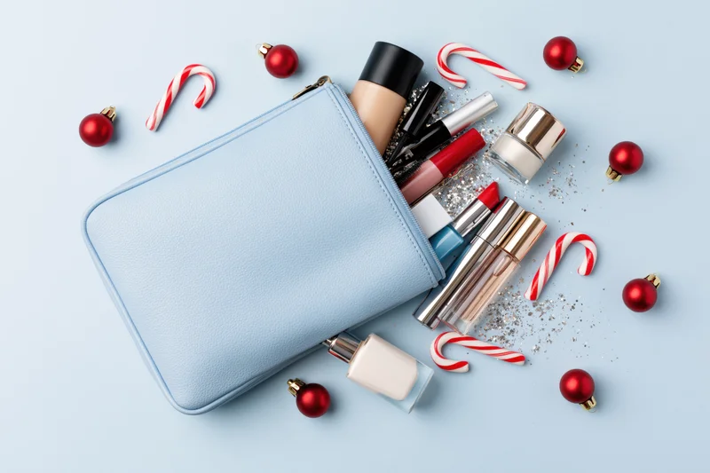 Light blue cosmetics pouch open with makeup products and holiday decorations on a blue background