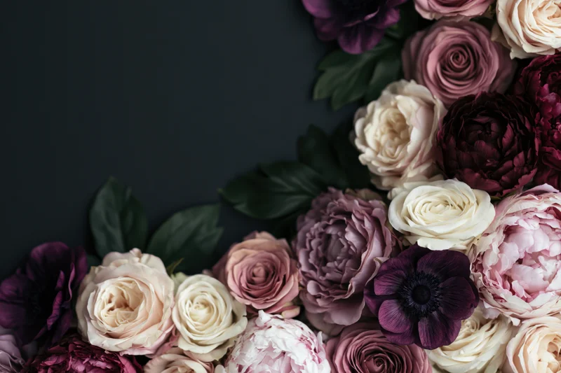 Lush floral arrangement of peonies, roses and anemones clustered in corner on dark background