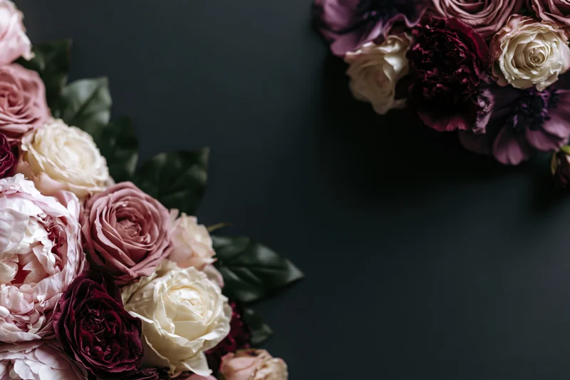Lush floral arrangement of peonies, roses and anemones on dark surface with copyspace