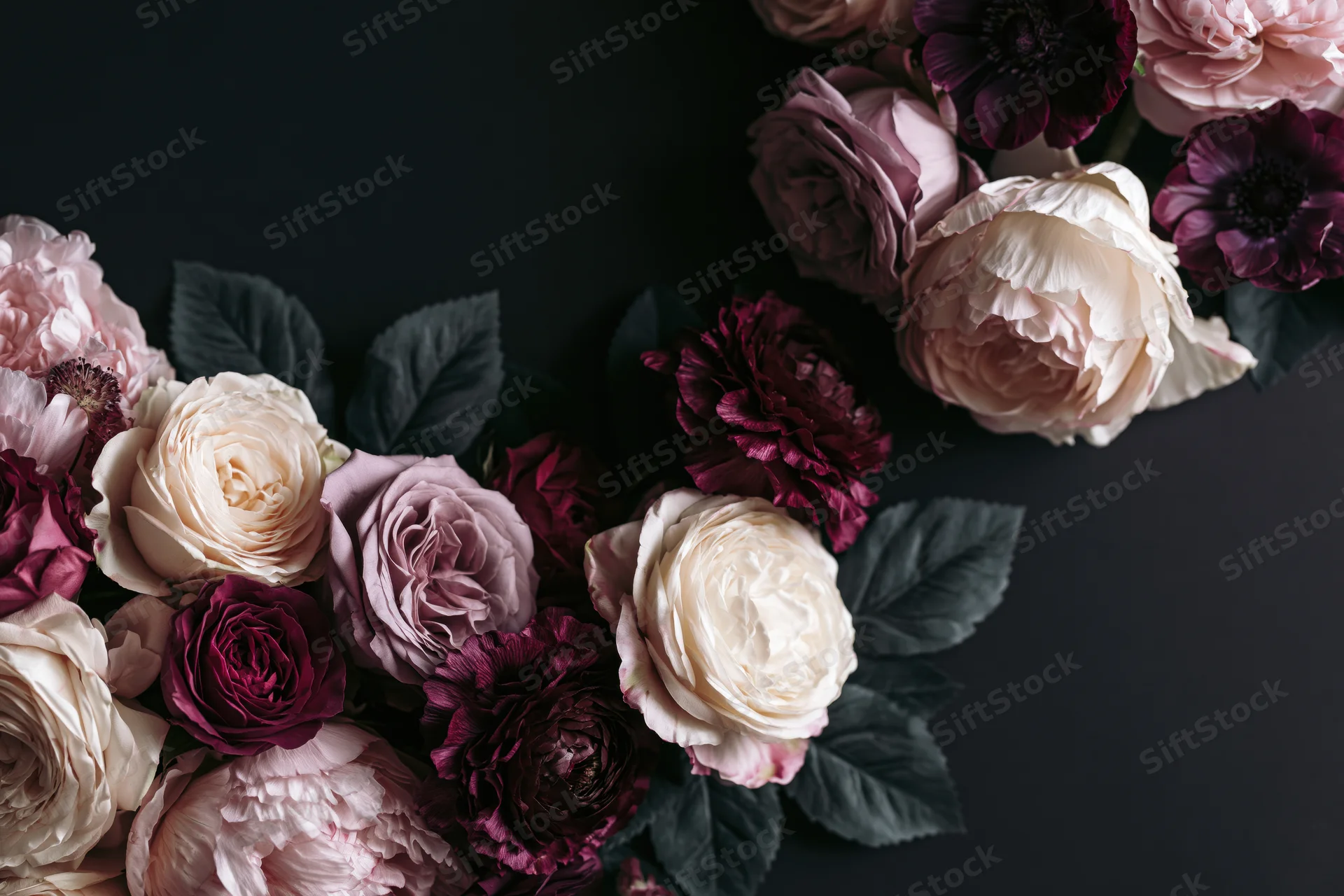 Lush arrangement of peonies, roses and anemones on dark background with copyspace