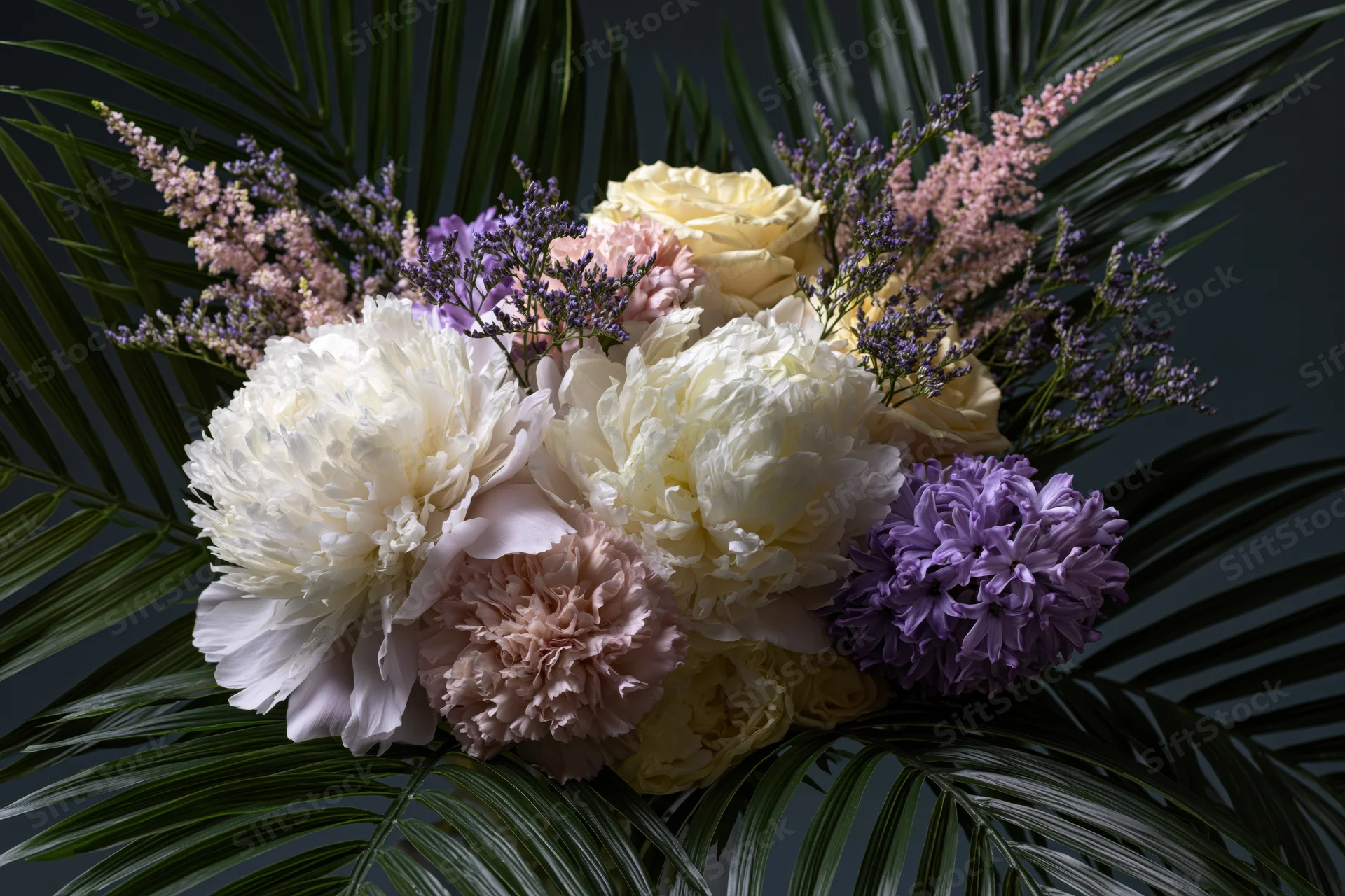 Lush floral arrangement with white and blush peonies, purple hydrangeas, and green palm fronds