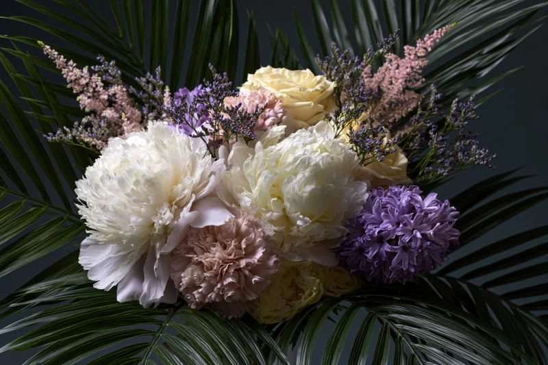 Lush floral arrangement with white and blush peonies, purple hydrangeas, and green palm fronds