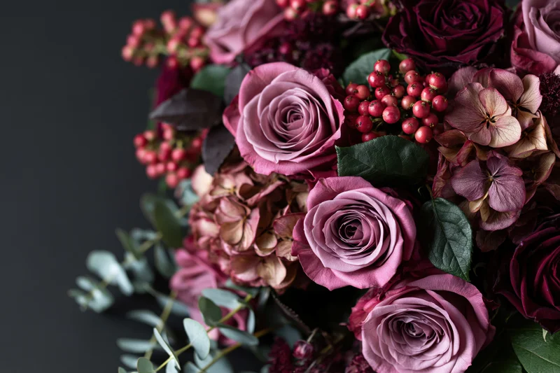 Lush bouquet of dusty pink roses and dried hydrangeas with eucalyptus and berries on dark background