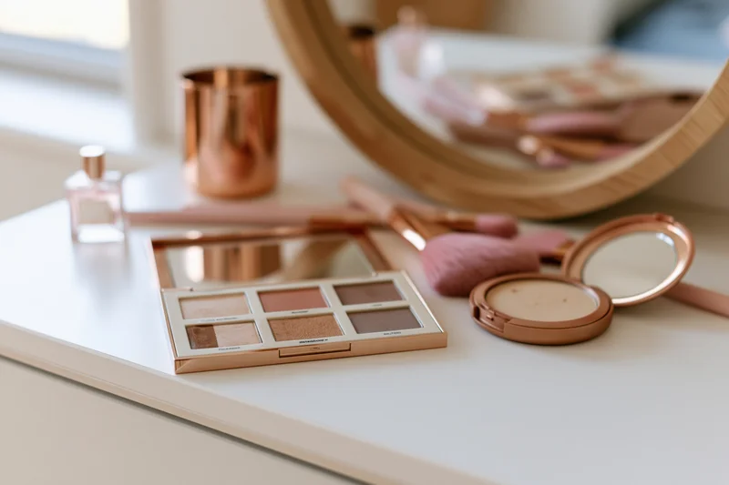 Makeup products arranged on a white vanity table with mirror and brushes