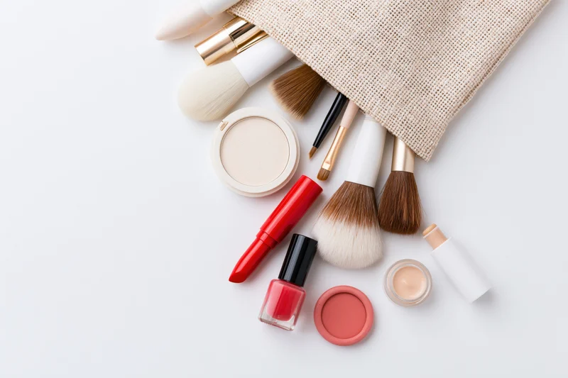 Makeup products spilled from a beige pouch on white surface
